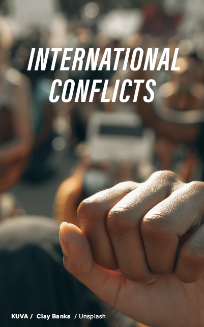 "Close-up of interlocked hands, portraying unity or tension, against a backdrop of a crowd, signifying international relations and conflicts."